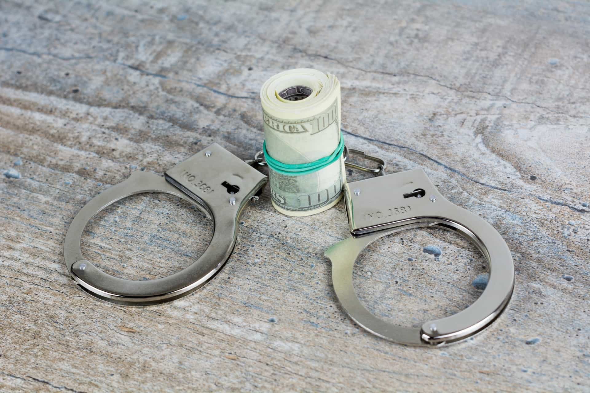 A pair of handcuffs next to a rolled up wad of cash.