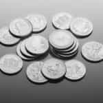 Numerous silver coins of varying currencies lying flat on a table.