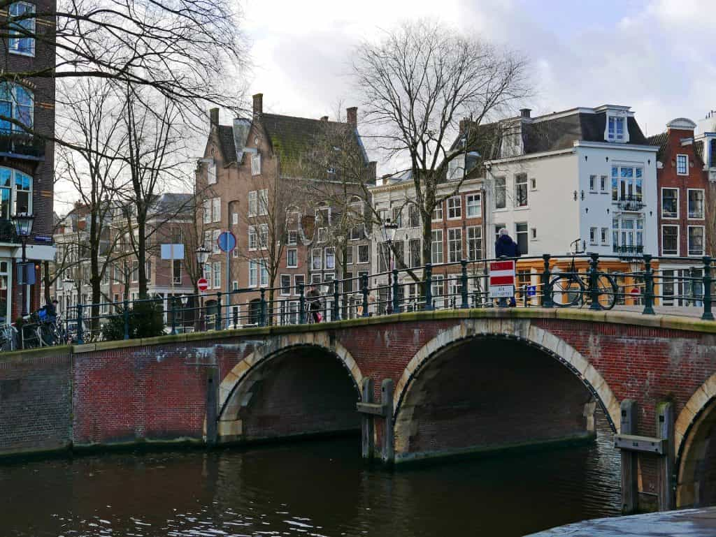 Old brick bridge over a water body with buildings in the background.