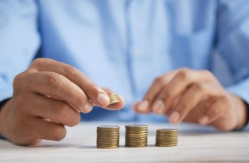 A person stacking coins in tiny piles on a table.