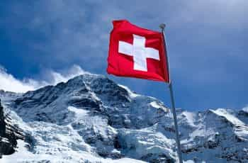 A red flag with a white cross hoisted near a snowy peak